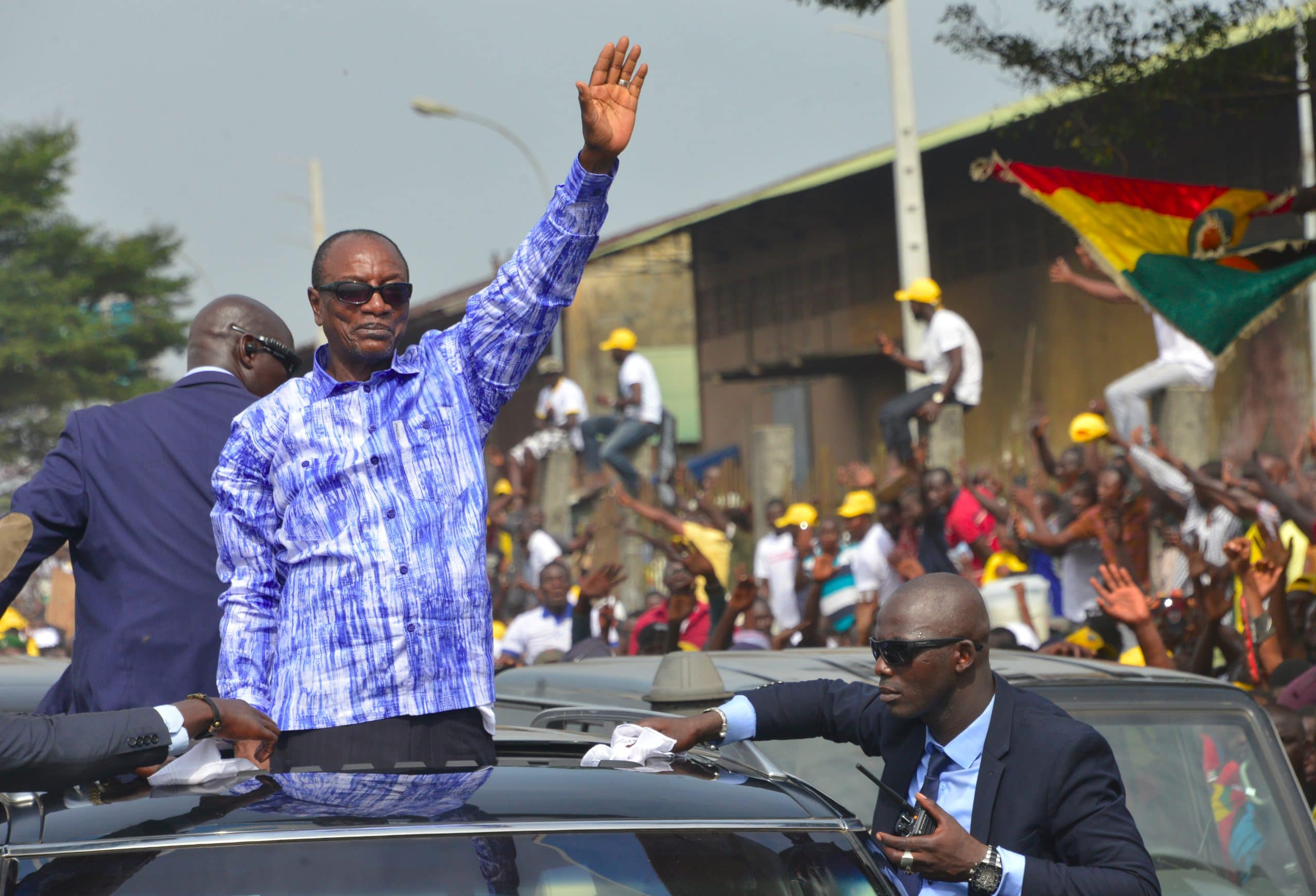 Dans cette photo d'archive prise le 31 octobre 2019, le président guinéen Alpha Condé salue ses partisans alors qu'il se tient dans un véhicule circulant sur une route à Conakry. - Le 31 août, le parti au pouvoir en Guinée a confirmé des mois de spéculation selon lesquels le président Alpha Condé briguerait un troisième mandat, une possibilité qui avait déjà déclenché des manifestations de masse meurtrières. La nouvelle est intervenue après que le président de 82 ans a fait adopter une réforme constitutionnelle en mars qui, selon les critiques, était déjà un stratagème pour lui permettre de se présenter à nouveau aux élections du 18 octobre.