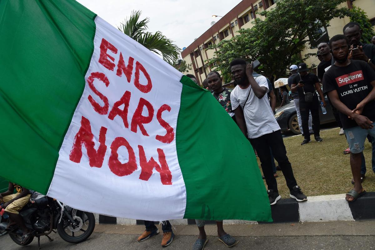 Des manifestants tiennent le drapeau national nigérian où quelqu'un a écrit "Ends SARS Now" lors d'une manifestation de protestation à Lagos, le 15 octobre 2020.